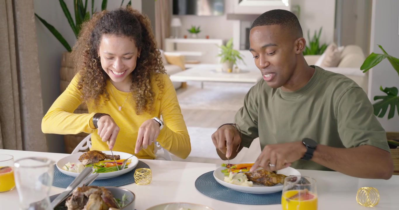 Casal diverso começando o jantar à mesa, cortando e provando carne assada com garfo e faca.