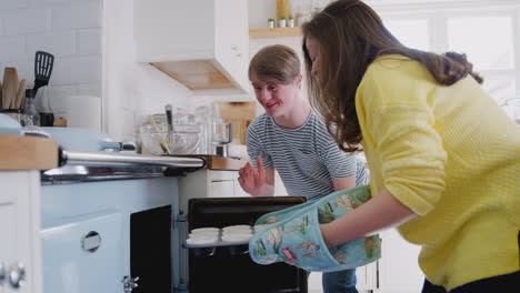 una pareja de síndrome de down pone pasteles caseros en el horno en la cocina de su casa.