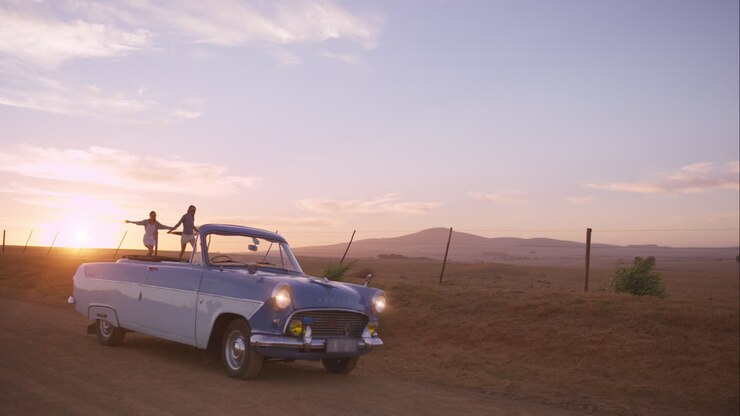 Amies dansant au coucher du soleil lors d'un road trip avec une voiture de collection.