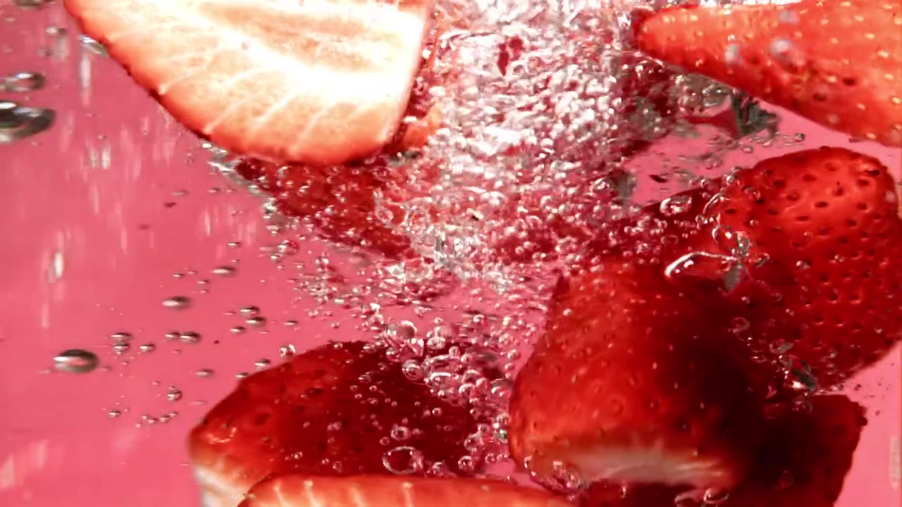 Zeitlupenaufnahme: Frisch geschnittene Erdbeeren fallen ins Wasser