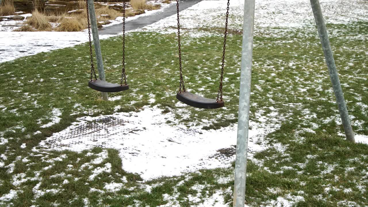 Empty swings hang in a snowy playground, evoking a feeling of solitude and winter stillness