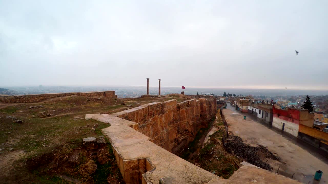 el foso hecho a mano del castillo de urfa divide las ruinas y los barrios marginales lejos dos columnas los pájaros vuelan la nieve y la lluvia