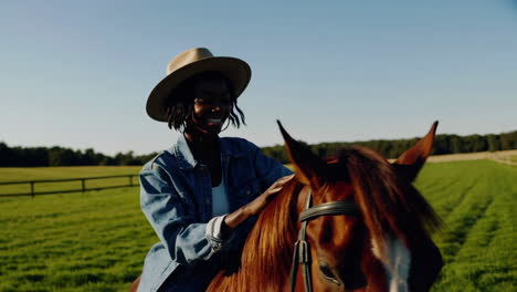 happy woman in a cowboy hat riding a horse in a sunny field