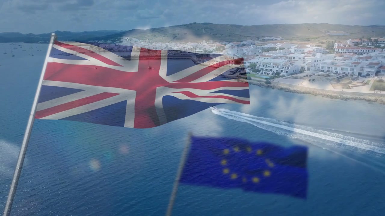 Tuulenpuuskat saavat Union Jack -lipun liehumaan ja EU-lipun aaltoilemaan, luoden pehmeän päällekkäiskuvan lahden vanavesien ylle