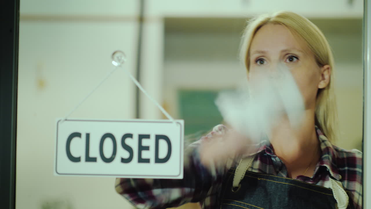 женщина средних лет протирает стеклянную дверь в магазине поздним вечером во время сверхурочной работы