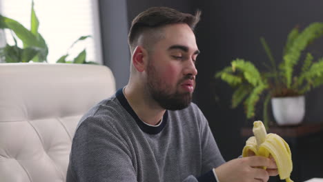 hungry man sitting at desk and eating banana