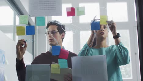 man and woman discussing over memo notes on glass board at office