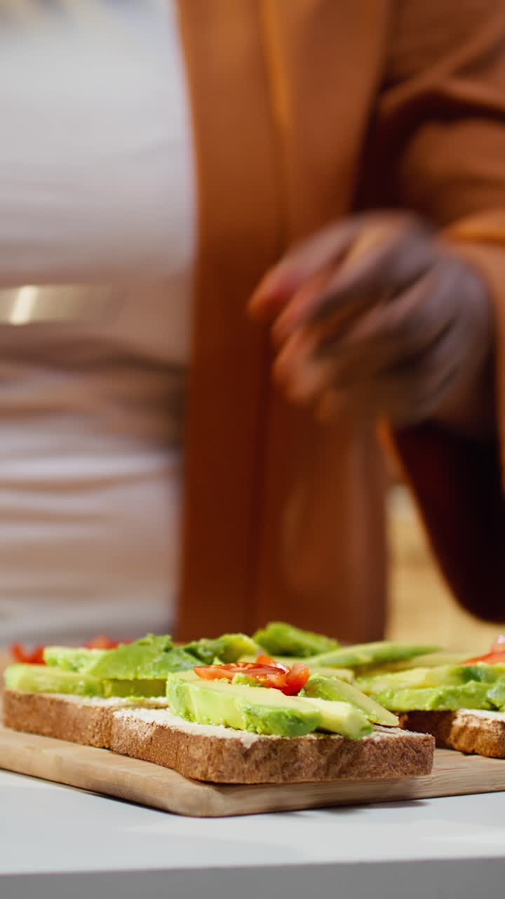 Video verticale: Chef donna afroamericana che taglia pomodorini e prepara avocado su toast.