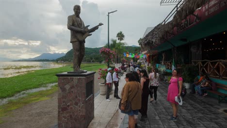 people at statue of singer mike laure on promenade of lake chapala at sunset in jalisco, mexico. static shot
