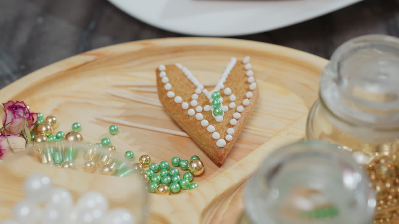 primer plano de cuentas decorativas verdes y doradas esparcidas alrededor de galletas decoradas en una bandeja de madera, galletas adornadas con glaseado blanco y cuentas en una hermosa exhibición artística