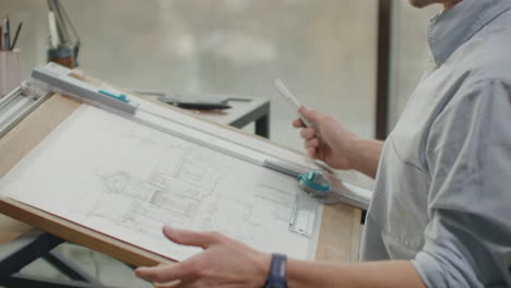 a male architect sitting at a table draws a plan of the building and is engaged in design development sitting in the office in the sitel loft near a large window.