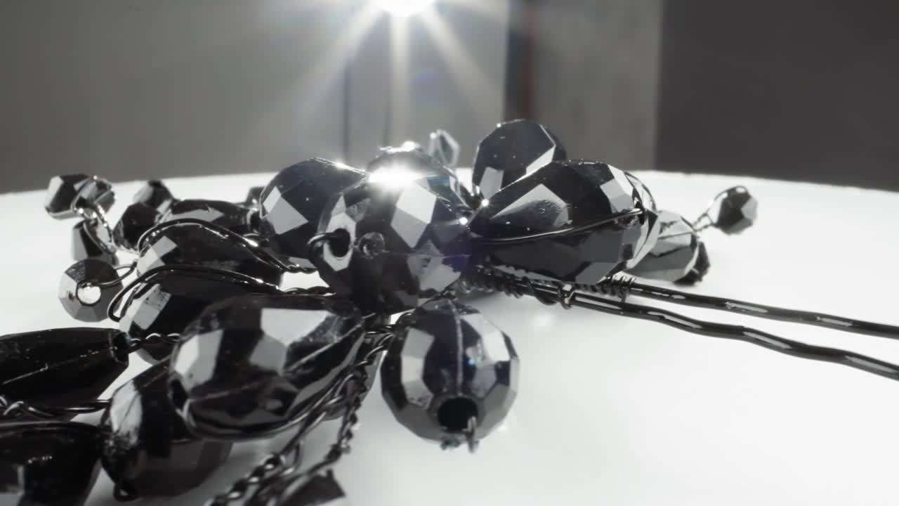 блестящее ожерелье из черного драгоценного камня на белой поверхности с яркой светлой вспышкой