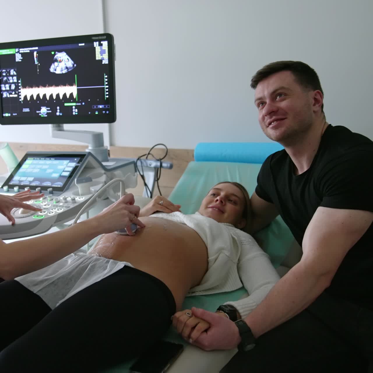 Happy expecting parents at the ultrasound examination. Husband supports his wife kissing her in forehead