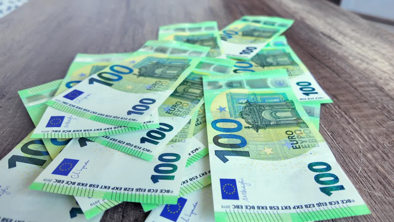 Grønne 100 euro-pengesedler falder ned på bordet.