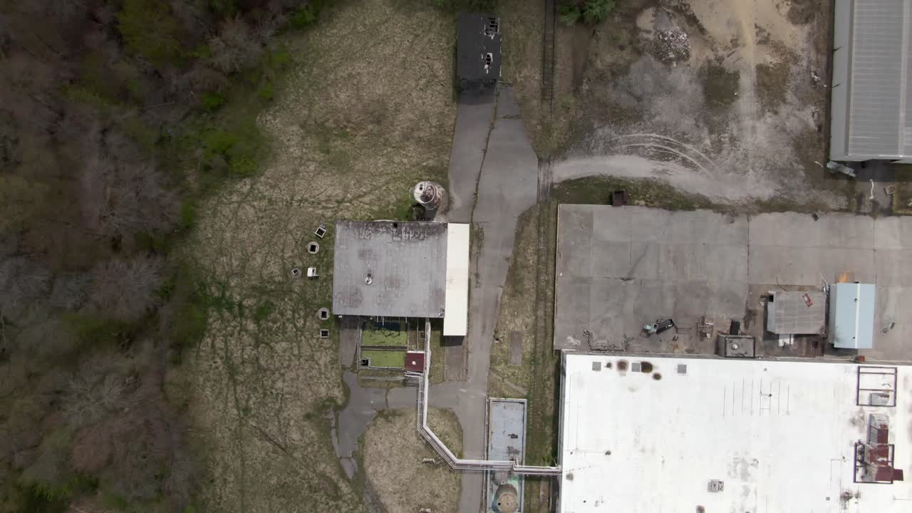 imágenes aéreas de drones de arriba hacia abajo que avanzan sobre una fábrica abandonada y en descomposición y edificios circundantes con agujeros en el techo