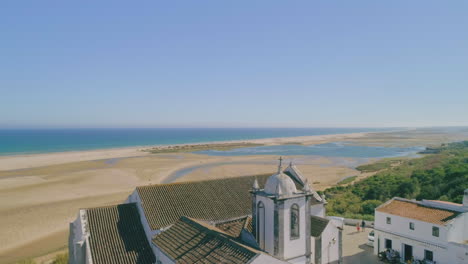 drone flyover historic cacela velha church towards ria formosa sandbanks and atlantic ocean, algarve