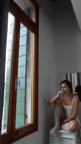 woman brushing teeth by the window