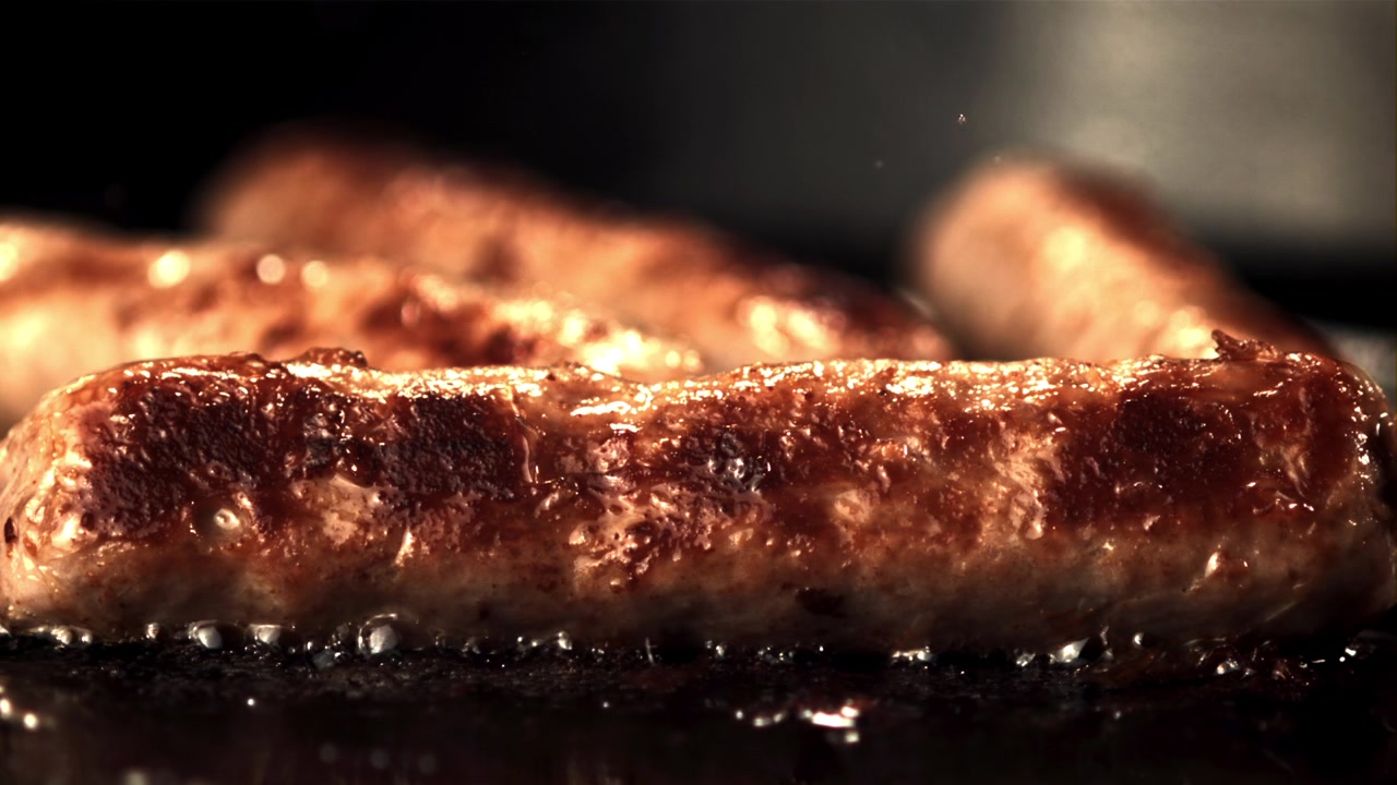 Gros plan de saucisses grésillant et friant dans une poêle chaude