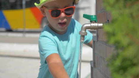 Boy-washing-your-hands-in-fountain-faucet-in-public-place-at-summer-day-Piraeus-Greece