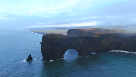Aerial-cinematic-drone-to-the-right-movement-stunning-sunrise-fog-mist-with-birds-flying-every-direction-early-winter-at-Black-Sand-Beach-Apostles-Dyhrolaey-lighthouse-and-cave-Reynisfjara-Iceland
