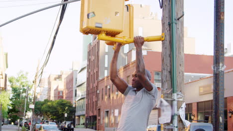 Young-black-man-doing-chin-ups-from-crossing-light-in-street