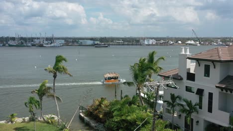 Fort-Myers-harbour-in-USA-from-above-with-boat-sailing-right-during-the-day,-palm-trees-in-summer