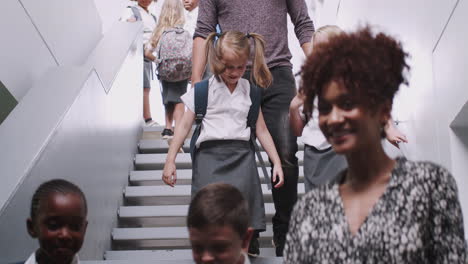 teacher and pupils walking down stairs in busy elementary school corridor