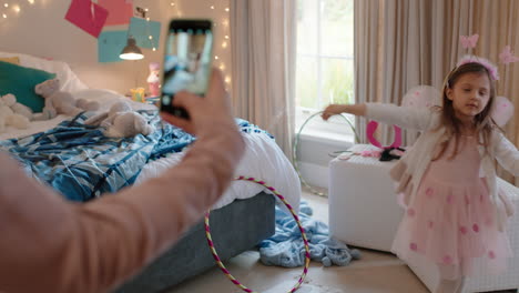 Una-Niña-Feliz-Jugando-A-Vestirse-Con-Un-Disfraz-De-Hada-En-El-Dormitorio-Con-Su-Madre-Tomando-Fotos-Usando-Un-Teléfono-Inteligente-Compartido-En-Las-Redes-Sociales