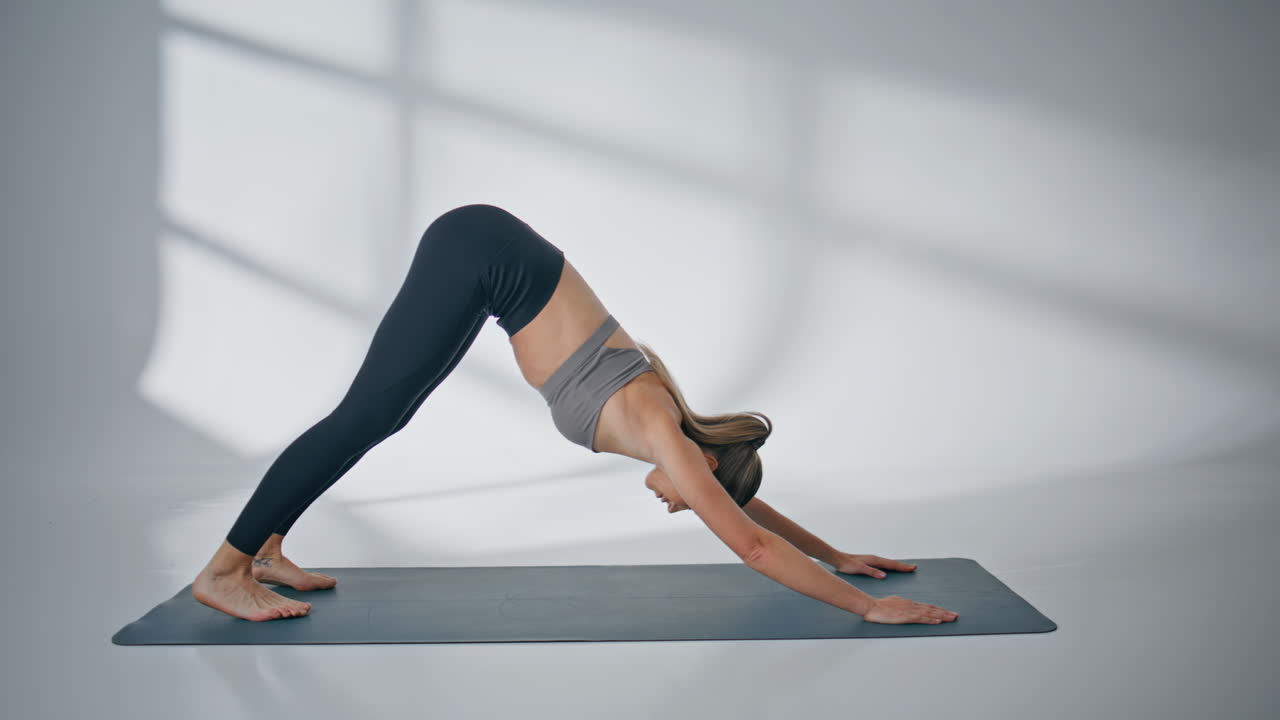 Sportliches Modell dehnt die Körpermuskulatur in der Pose des nach unten schauenden Hundes in einem hellen Studio