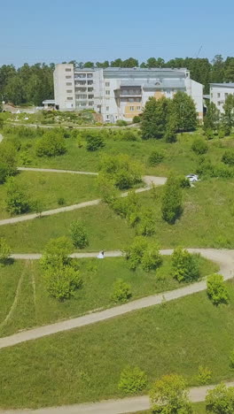 distant just married couple walks along path with hairpin curves on green steep hill on nice sunny day aerial view