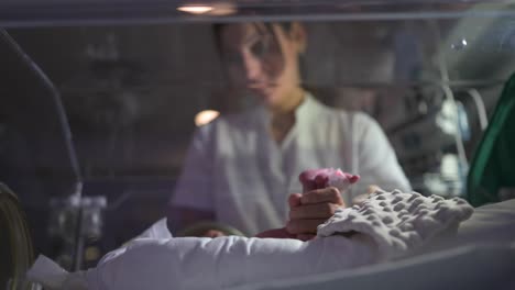 Nurse-gently-touching-fragile-newborn-in-neonatal-incubator