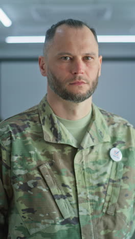 retrato de soldado masculino, votante de las elecciones de los estados unidos de américa. hombre en uniforme de camuflaje se encuentra en una estación de votación moderna y mira a la cámara. fondo con cabinas de votación. concepto de deber cívico.