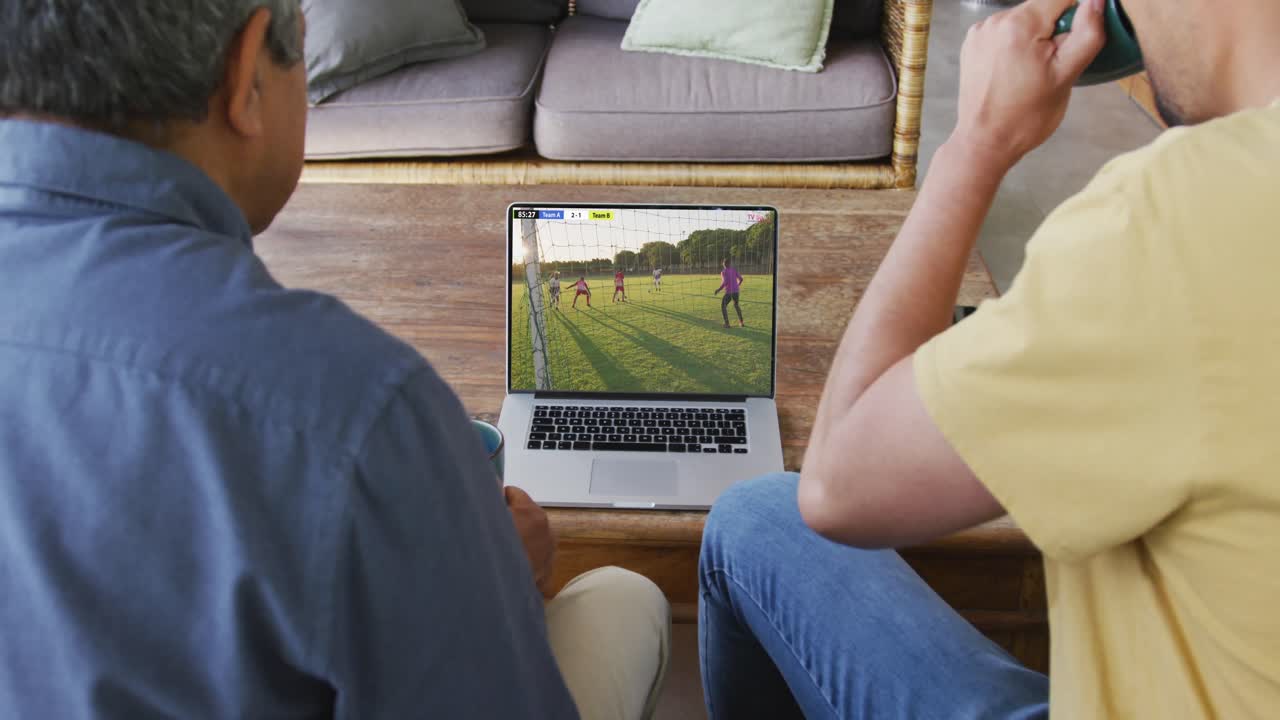 video de varios amigos hombres sentados en el sofá y viendo fútbol en la computadora portátil en casa