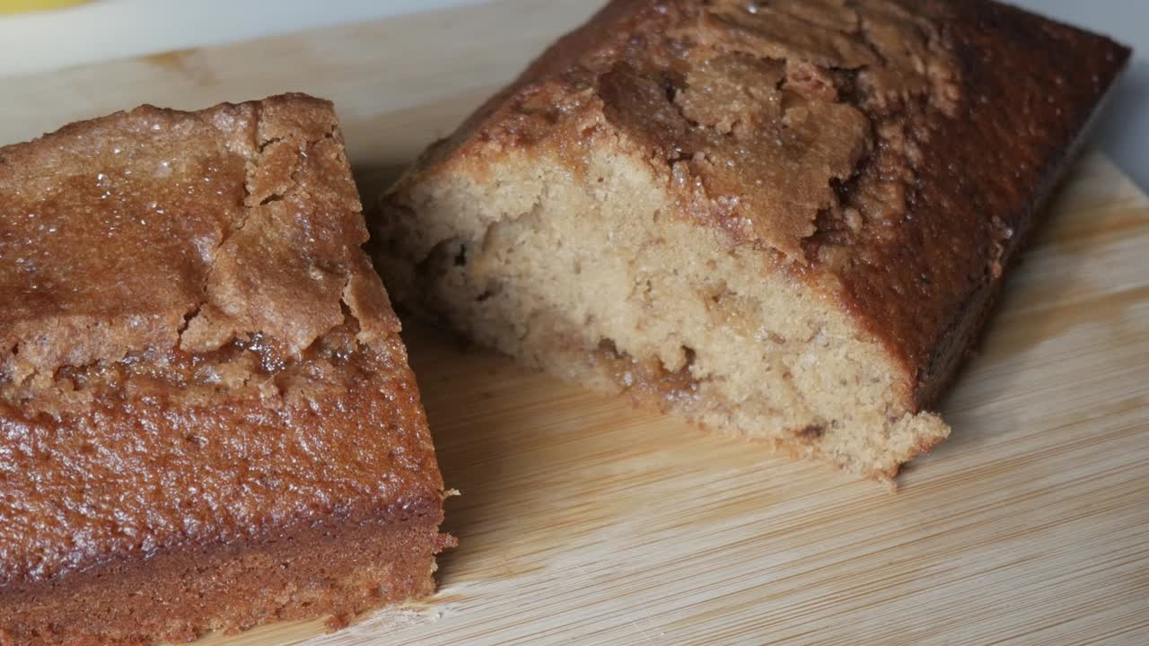 Zoom out shot of freshly baked banana bread loaf sliced on wooden board showing texture