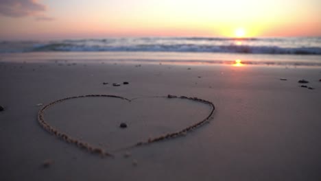 Heart-symbol-drawn-on-sand-against-a-backdrop-of-sunset-over-the-sea