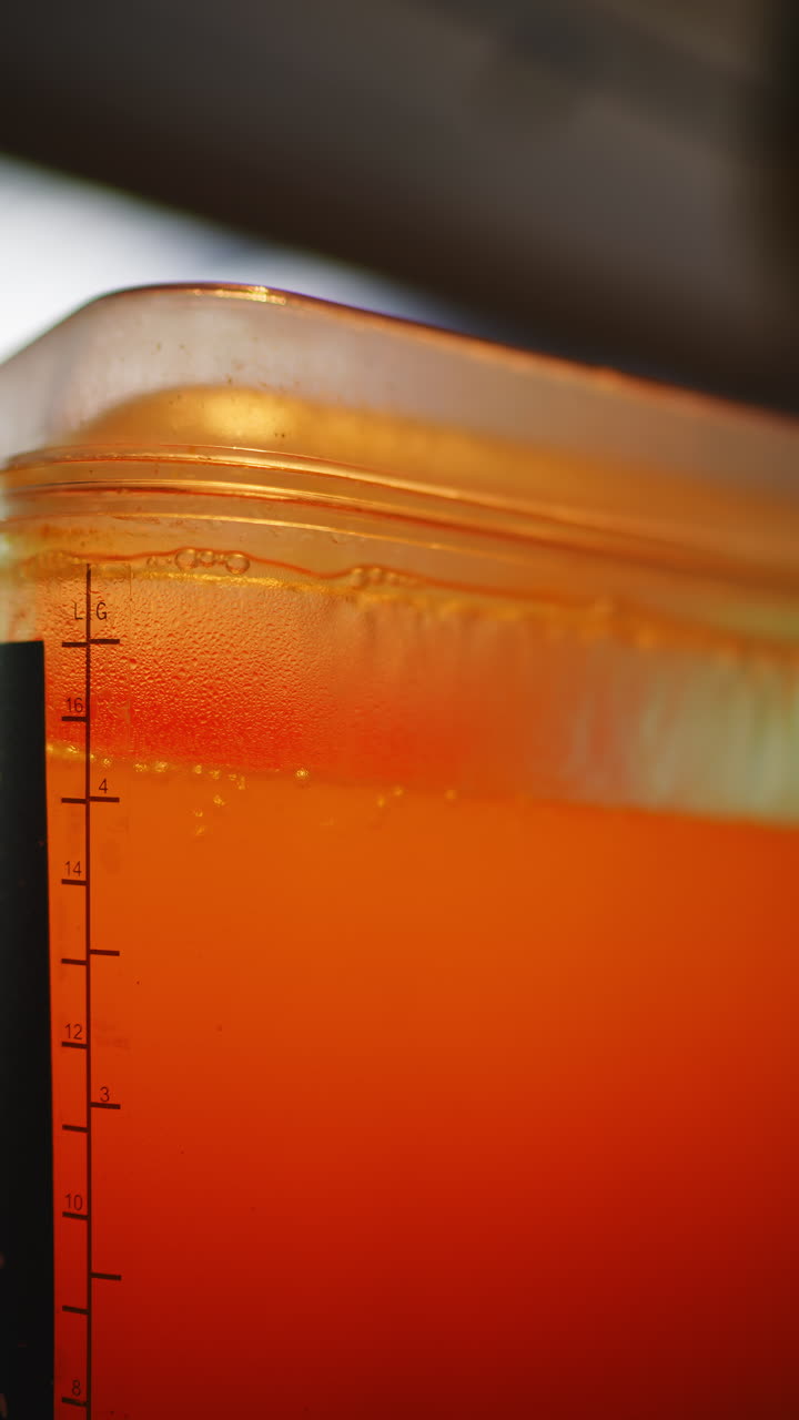 Liquido arancione vivace che si deposita in un contenitore di misurazione trasparente.