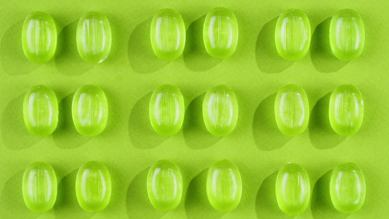 Green mint mentol lollipops, candies, bonbons disappear on purple background. Summer bright texture studio shot for store, supermarket, close up top view. Children favorite sweets made of sugar.