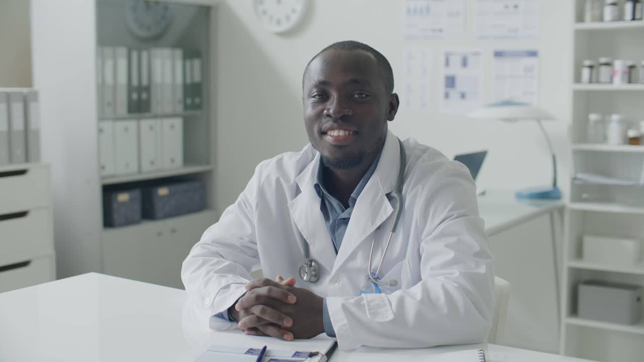 Portrait of Smiling Black Doctor at Desk in Modern Medical Office