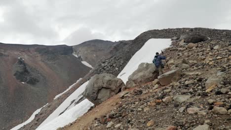 Male-hiker-climbing-on-rocky-slope-of-Mount-Asahidake-in-Japan-during-cloudy-day