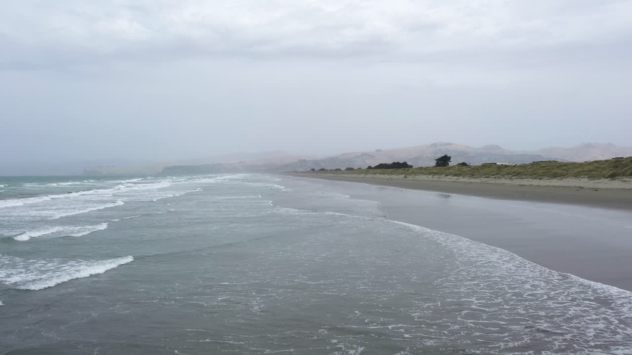 Aerial shot flying over waves towards a dark stormy sky.