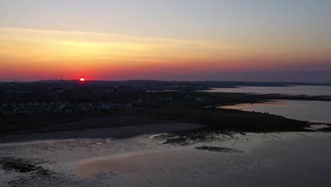 Golden-sun-rises-above-orange-and-pink-horizon-over-Galway-Bay,-Grattan-beach-at-low-tide,-Galway-Ireland