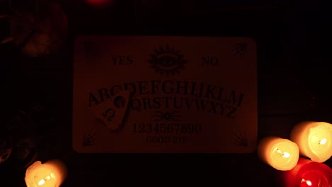 close up video of a wooden ouija board on a table surrounded by candles and a cross in a muffed close up video of a wooden ouija board on a table wax candles and a cross around the planchette is slowly moving across the board spelling out words and numbers creative mystical content