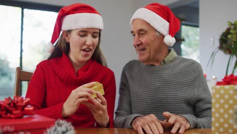 Glücklicher-Kaukasischer-älterer-Vater-Und-Erwachsene-Tochter-Mit-Weihnachtsmützen,-Die-Ein-Videoanruf-Eröffnungsgeschenk-Machen
