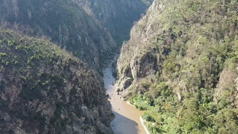 aerial descends deep rocky canyon to group of rafters on snowy river