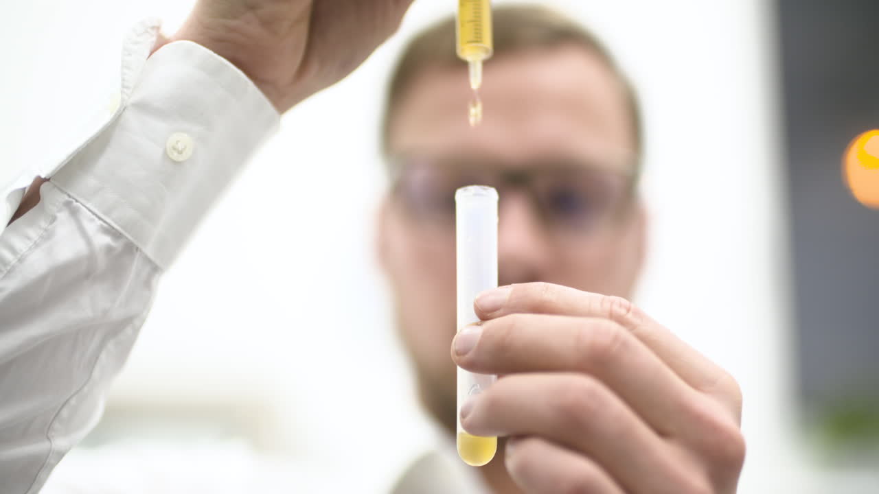Scienziato che versa liquido giallo in una provetta in laboratorio.