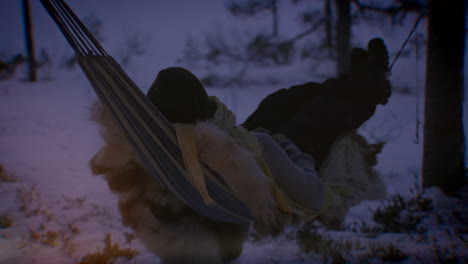 a person laying on reindeer skin in a hammock with flares from a fireplace during wintertime