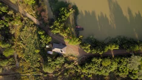 Vista-Aérea-De-Arriba-Hacia-Abajo-De-Una-Casa-Rural-Independiente-Aislada-Con-Panel-Solar-Cerca-De-Un-Lago-Al-Atardecer