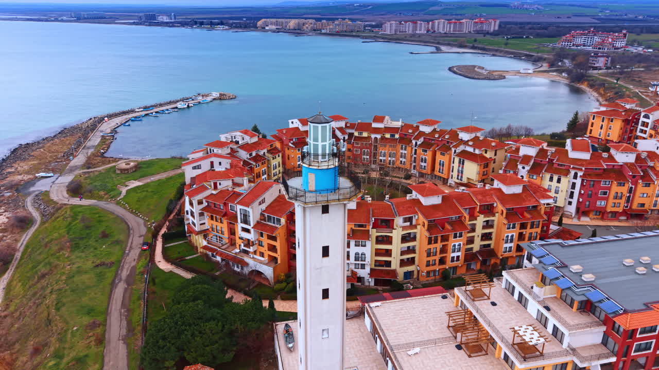 Vista aerea di una torre faro e di un quartiere residenziale. Scatto dall'alto incentrato su una torre faro bianca con un'area residenziale dai tetti rossi sullo sfondo.