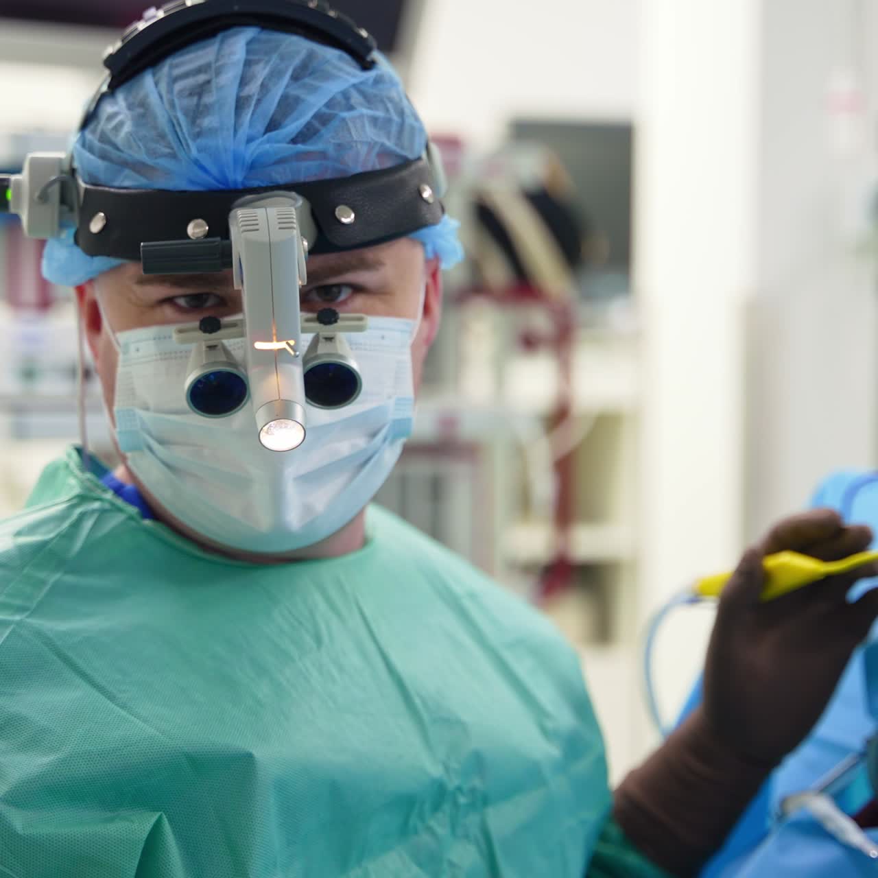 Male doctor wearing device glasses on his head talks to the camera. Surgeon holding an instrument in hand ready to apply it. Close up