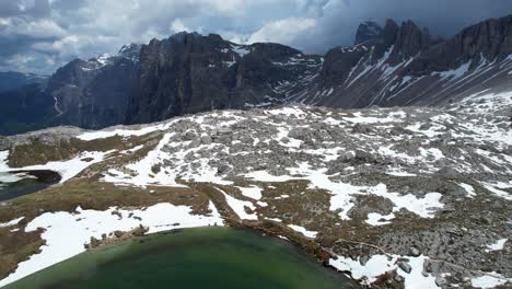 Aerial-backward-motion-reveals-thawing-ice-on-alpine-lake-near-rugged-mountains